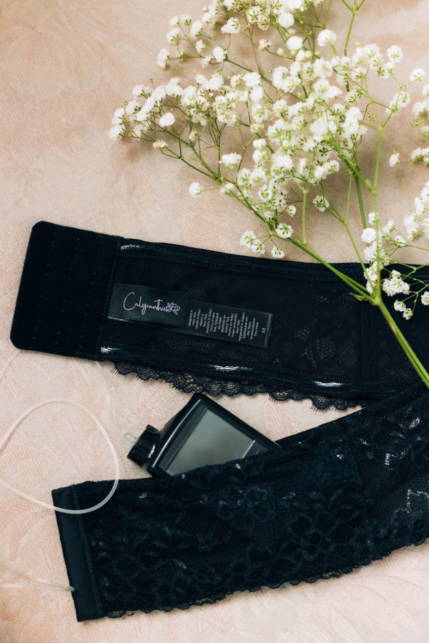 Black lace band with pocket to store insulin pump, laying on pink background with white flowers